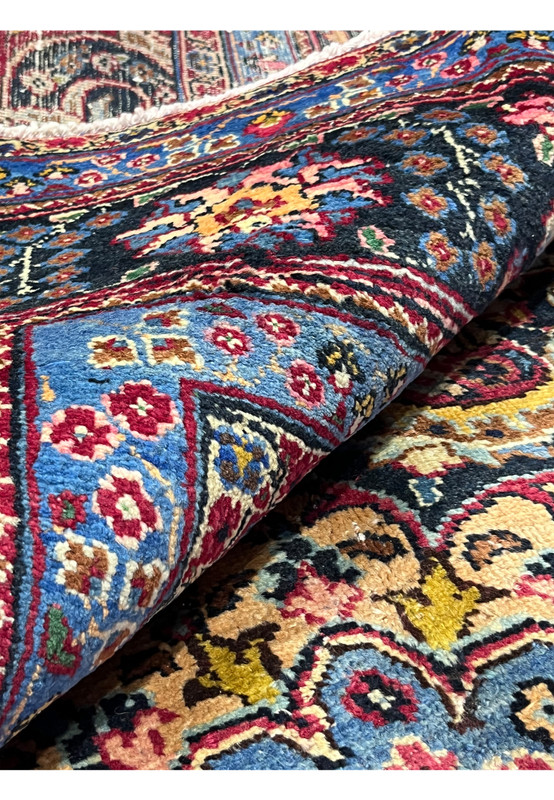 Persian Kerman rug shown rolled at the edge revealing handmade pile depth and bound selvage on hand-knotted wool