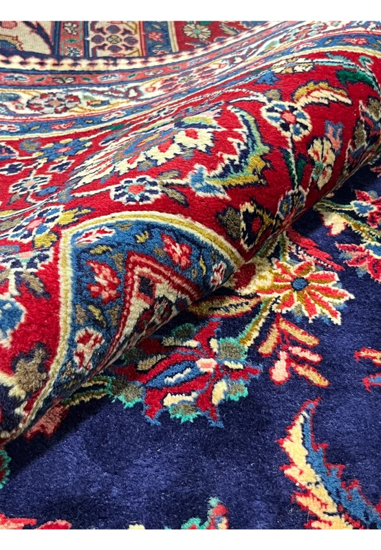 Folded view of Persian Qum kork rug showing kork wool pile depth and saturation across navy field and crimson border