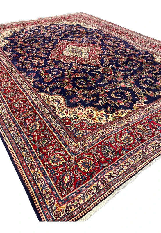 Angled studio view of Persian Qum kork rug, midnight navy field and crimson border holding the medallion in perspective