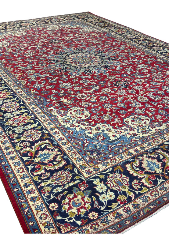 Angled view of Persian Najafabad rug, ivory guard stripes and navy palmette border framing cherry red field, handmade