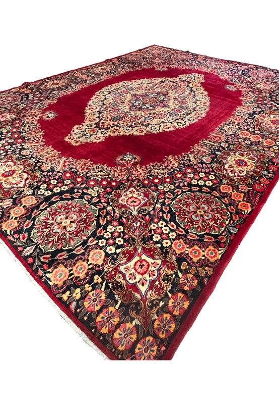 Angled view of 10x14 antique Persian Moud rug, signed Goliabadi workshop, ivory medallion on deep red, for formal dining room