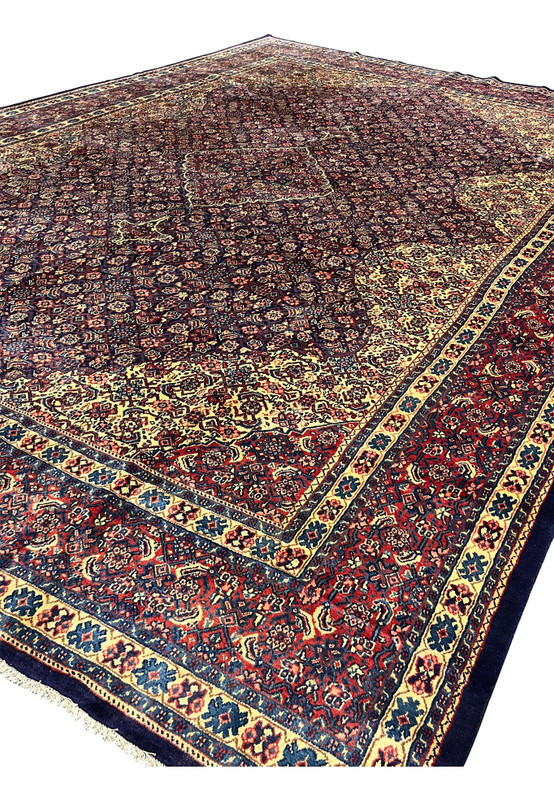 Angled view of oversize 10x15 Persian Sarough rug, navy field and salmon boteh with red border, hand-knotted for large dining room