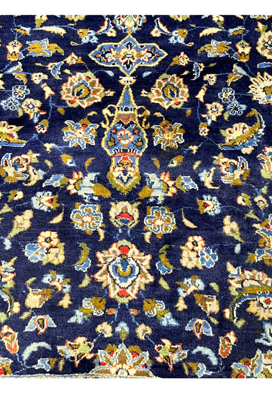Color and pattern closeup of Kashan rug with gold, green, and terracotta blossoms on navy wool pile