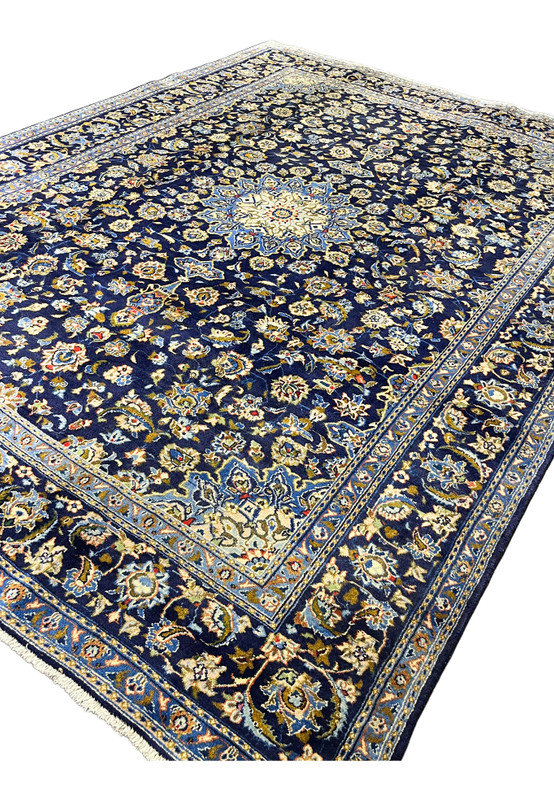 Angled view of authentic Persian Kashan rug showing navy field, ivory medallion, and floral border depth