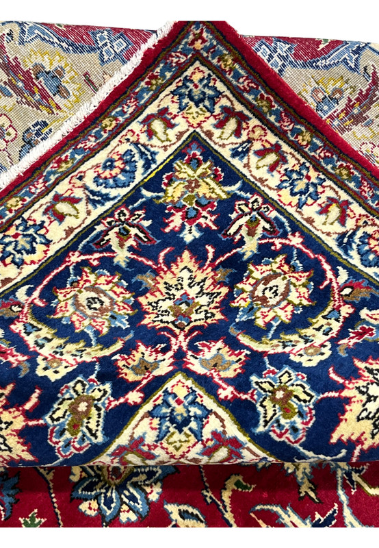 Folded edge of authentic hand-knotted Najafabad rug revealing cotton foundation and red selvage