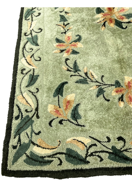 Border corner of sage green hand-hooked rug with curling leaf scrolls and floral buds