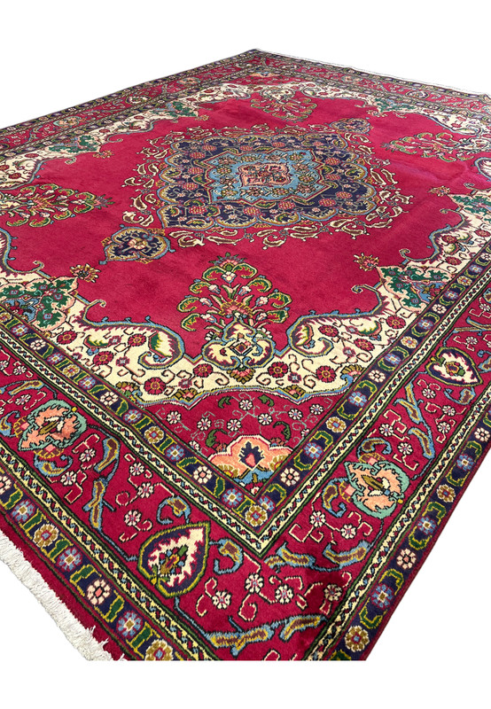 Angled view of large Persian Tabriz wool rug, red field traditional medallion design for spacious living room