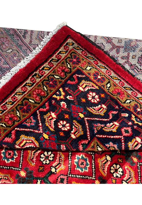 Folded corner showing the cotton foundation reverse beside the navy floral border and red wool face
