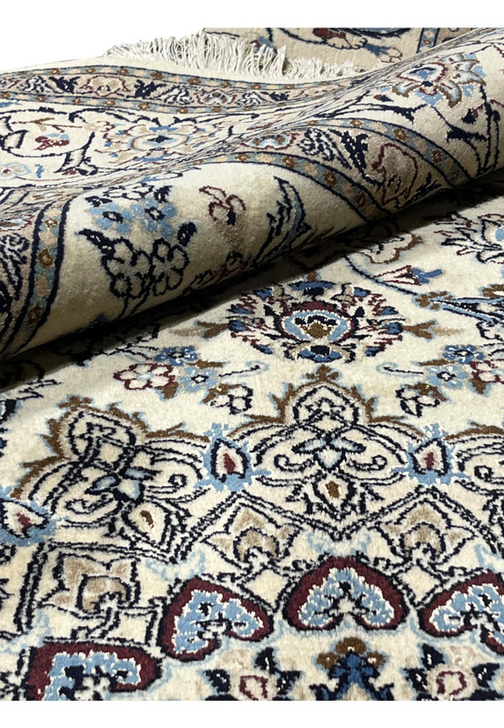 Folded Nain rug showing dense wool and silk pile with silk sheen across the medallion design