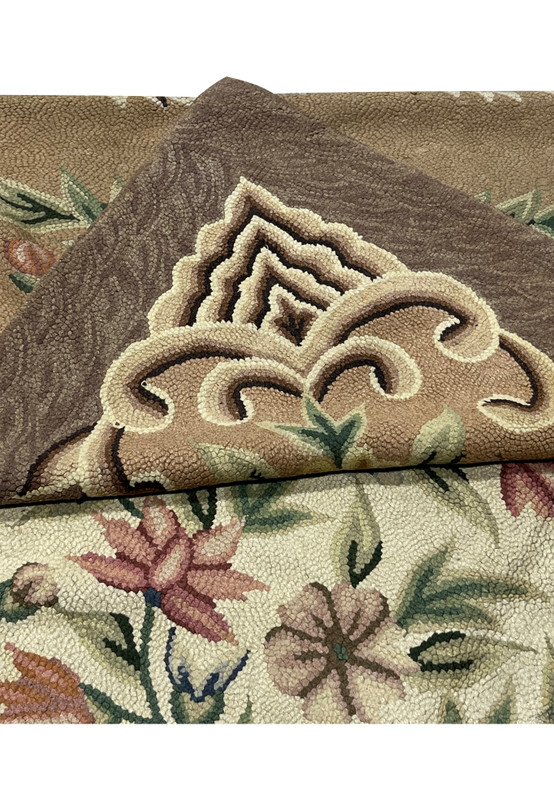 Folded corner showing the cream scroll cartouche and floral field of this hooked Oriental rug