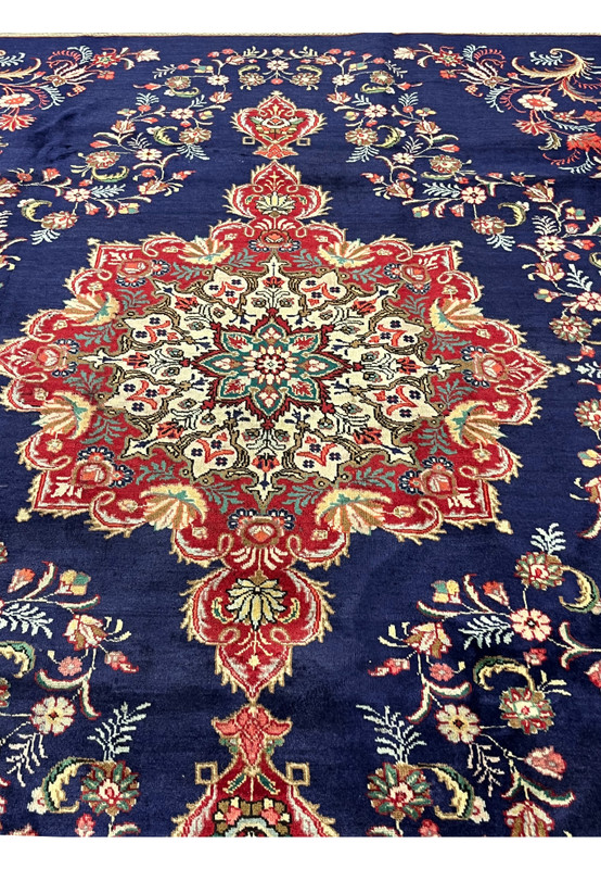 Red and ivory floral medallion with a green starburst center anchoring the deep navy Tabriz field
