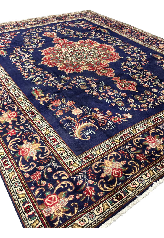 10x13 Persian Tabriz rug at an angle showing the navy field, red medallion and floral border
