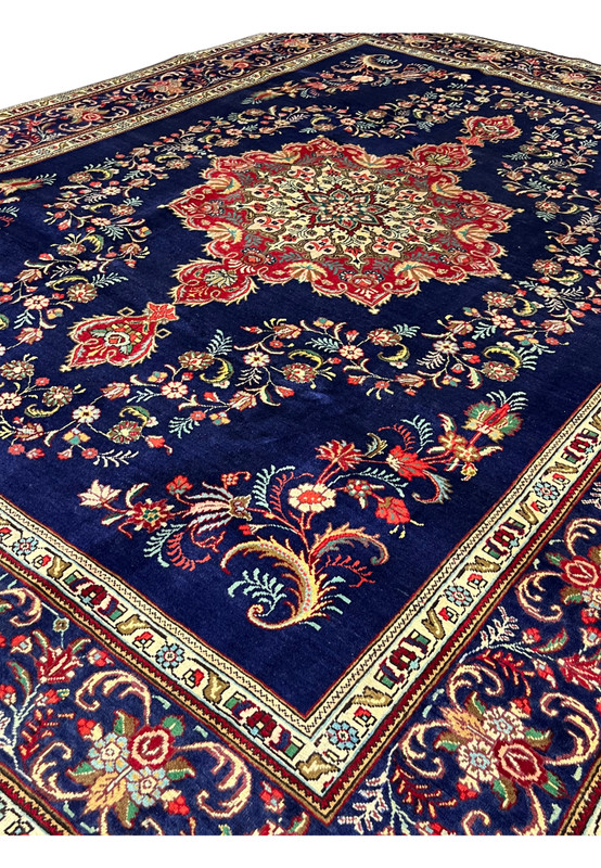 Persian Tabriz carpet seen from the side with its red medallion glowing against midnight blue wool