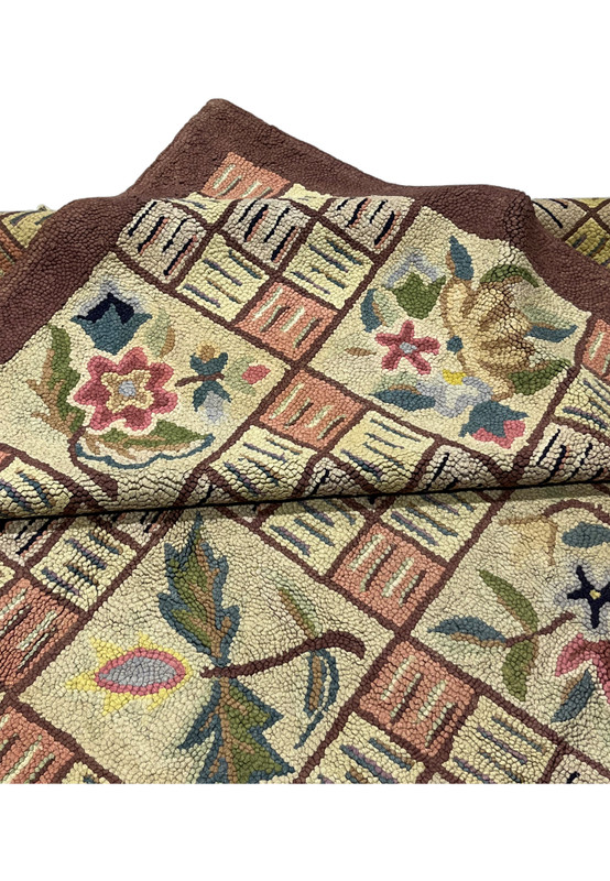 Folded edge of the hooked rug showing the brown border and plush loop pile