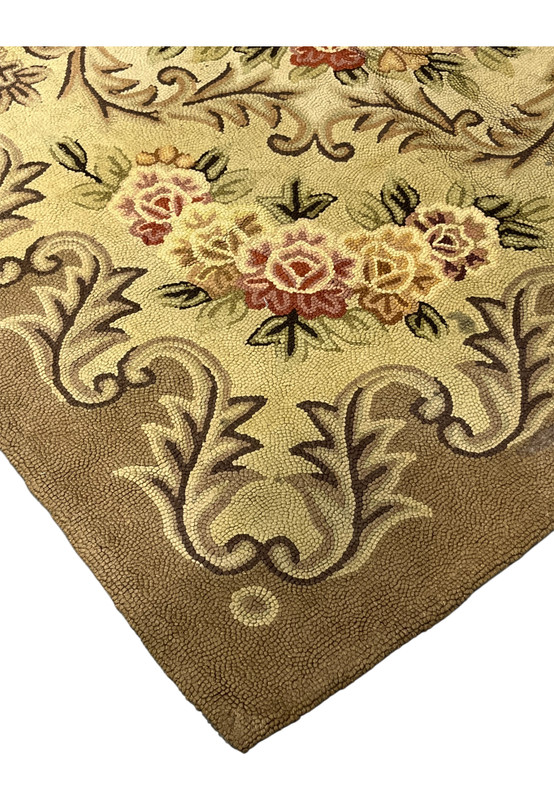 Corner detail of the mocha border with pale acanthus scrolls and a rose cluster on the hooked wool