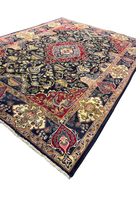 Angled view of the 8x11 Kashmar Zirkhaki rug showing the navy archaeology field and red border