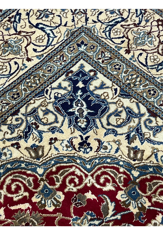 Close-up of red Persian Nain rug showing dense floral pattern with ivory, navy, and light blue detailing