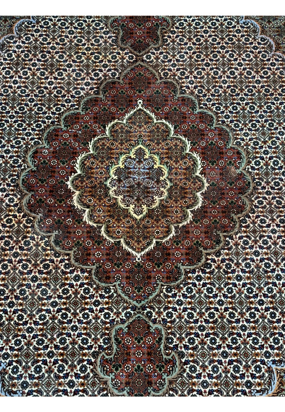 Detailed view of the central medallion of a Persian Tabriz Mahi rug, emphasizing the dense floral pattern and rich color palette on a dark field, with highlights of silk giving a subtle sheen.