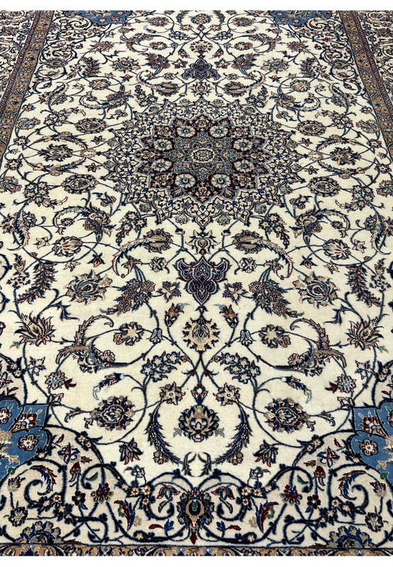 Top-angle view of a Persian Nain 4 LA Habibian rug showing luminous ivory field, navy floral motifs, and ornate royal blue corner designs.