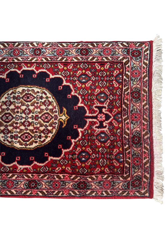 Close-up of Persian Bijar runner’s top corner showing crimson field, navy medallion, ivory border, and fine sky-blue floral detail.