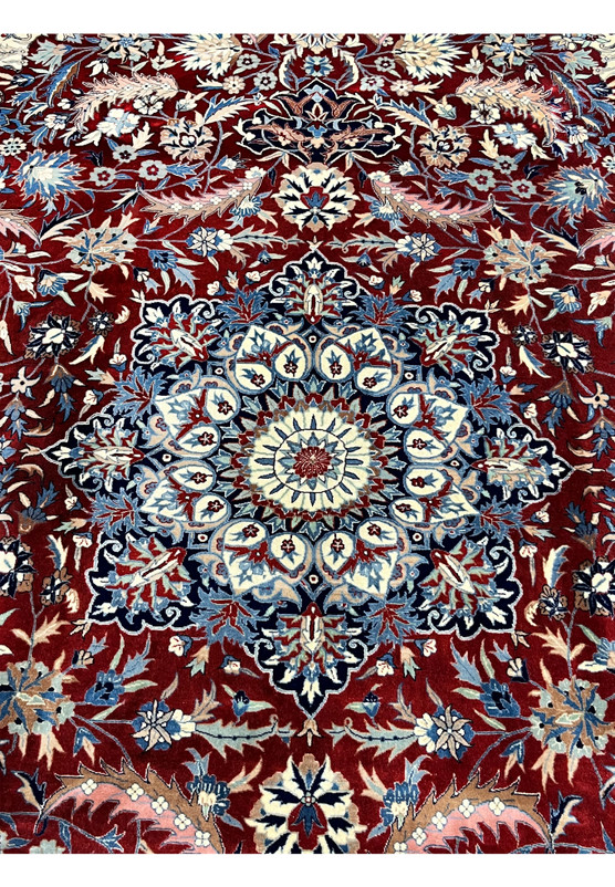 Central medallion of Persian Isfahan rug with layered floral rosettes, ivory and light blue highlights on a deep red background