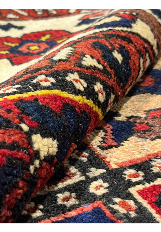 Rolled Persian Bakhtiar rug showing thickness, flexible wool pile, vibrant red and navy colors, and sturdy hand-knotted construction