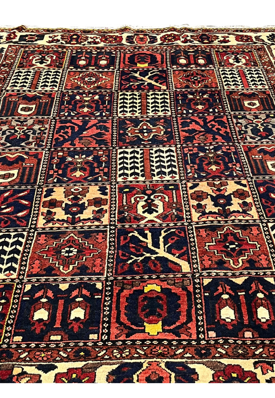 Midfield detail of a Persian Bakhtiar garden pattern rug highlighting pictorial square panels with tree motifs, floral symbols, navy blue grounds, and red accents