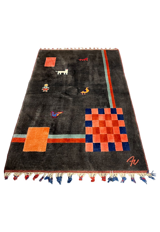 Laid down view of Persian Gabbeh rug showing minimalist tribal figures, dark charcoal background, coral stripes, and plush hand-knotted wool
