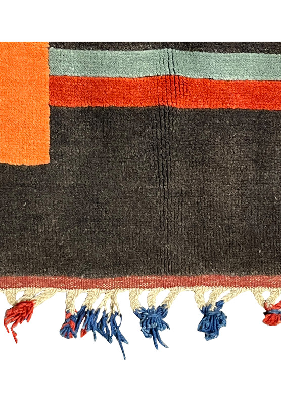 Persian Gabbeh tribal rug detail showing dark charcoal wool field with orange stripe and sage green band plus red and blue hand tied tassels