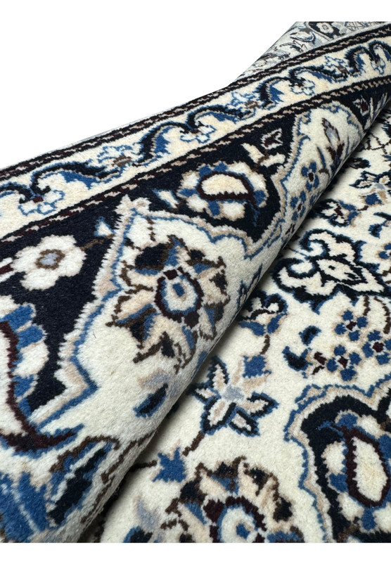 Rolled view of 3x5 Persian Nain rug showing wool pile depth, ivory ground and navy border flowing along the roll