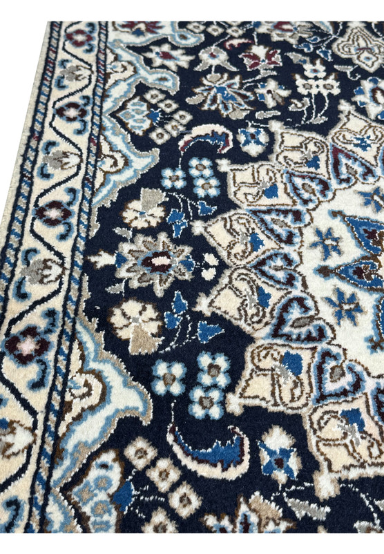Close-up of fine Nain knotting showing small blossoms and arabesques in blue, ivory, and wine