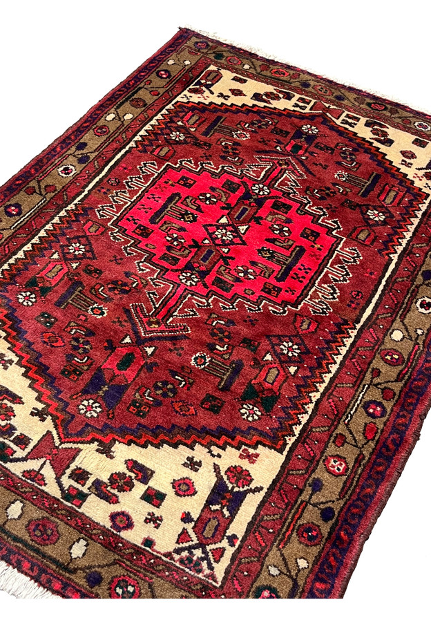 Angled perspective of a small antique Persian Hamedan rug emphasizing depth of color, bold medallion geometry, and authentic tribal village character