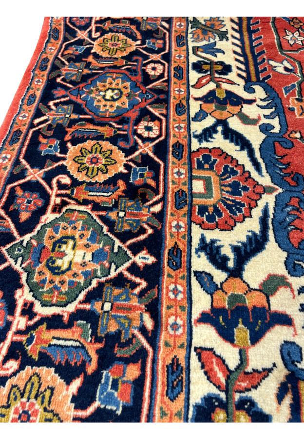 Close up of Persian Heriz rug border with rosette motifs, navy background, and precise hand knotted construction