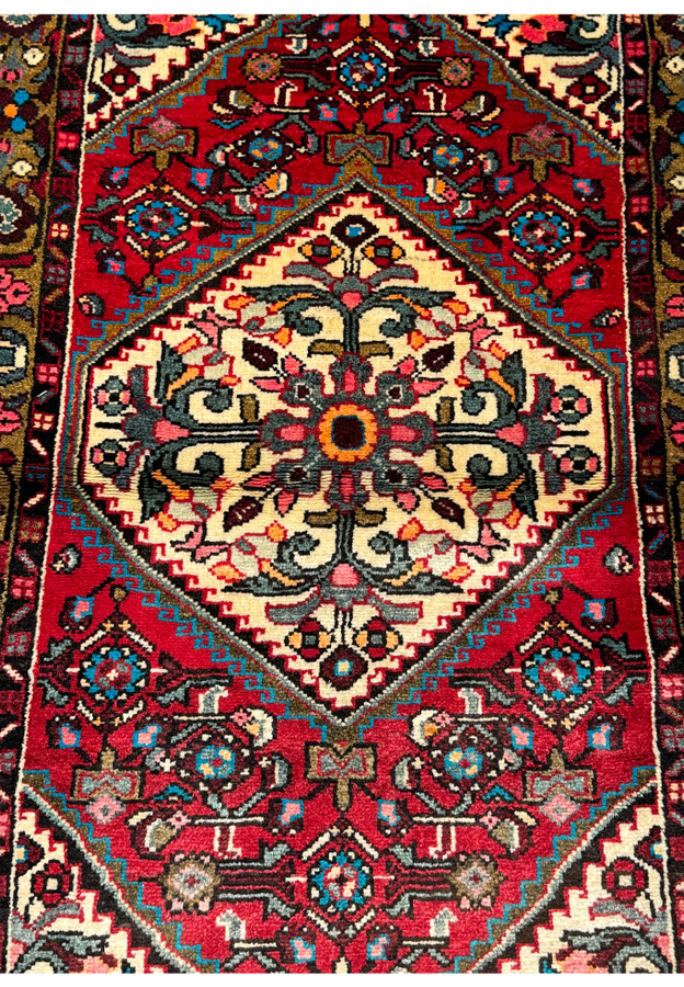 Close-up of the central medallion and floral patterns on a Persian Hamedan rug against a crimson background