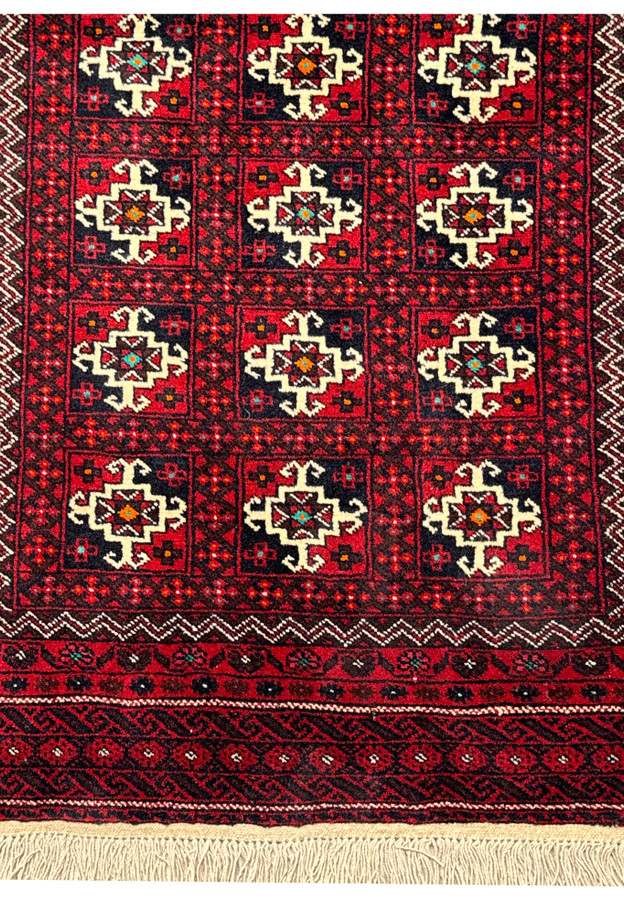 Full view of a Persian Baluch area rug, emphasizing the rich red field, traditional motifs, and natural wool fringes.