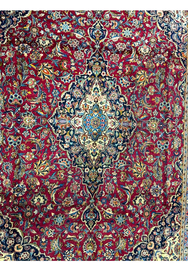 Close-up of the intricate and colorful floral designs against the burgundy background of a Persian Kashan rug