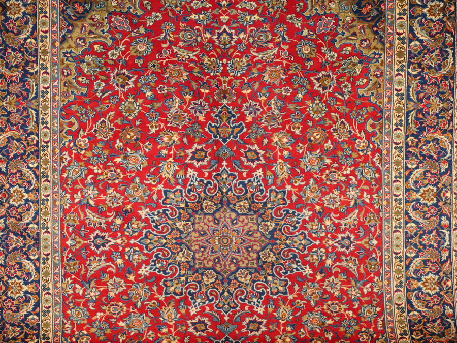 Close-up perspective of the Persian Isfahan rug's midfield, showcasing the central medallion's complex design, surrounded by a lush field of intertwined floral patterns in shades of blue, gold, and cream