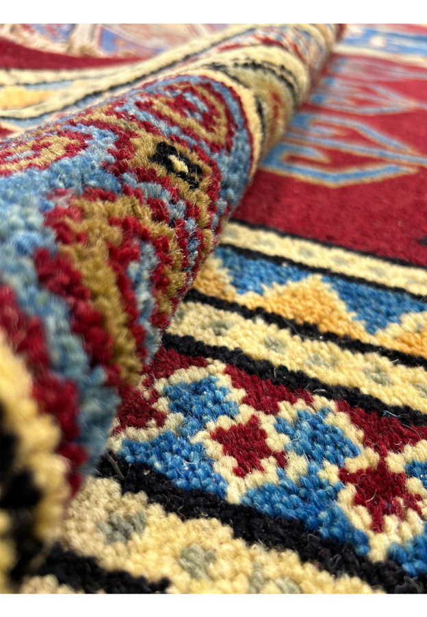 A close-up shot highlighting the fine texture and weave of the rug. The focus is on the intricate details of the pattern, showing the individual threads and knots in shades of blue, red, and cream.