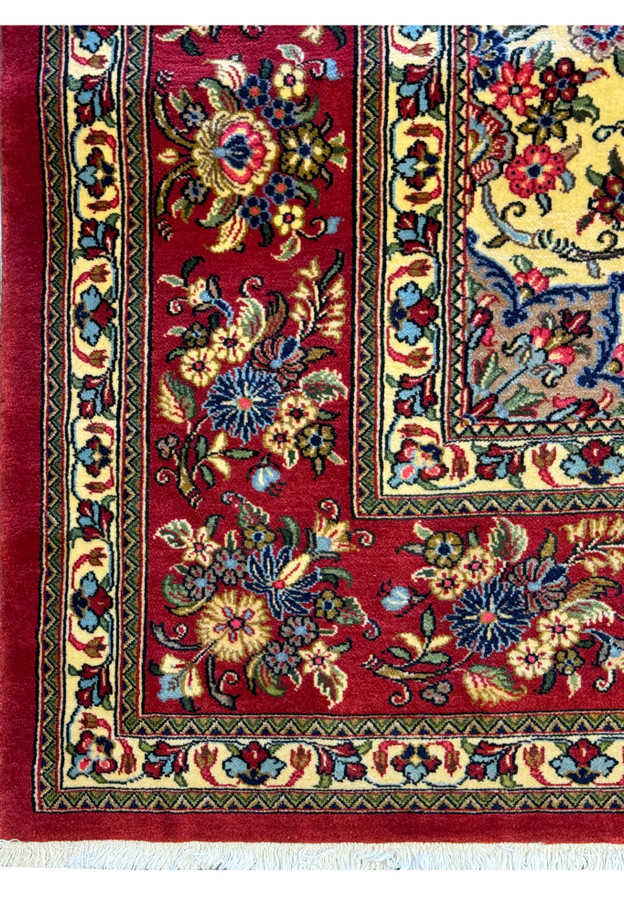 Detailed image of the corner border of a Persian Qum Kork rug, featuring rich red background with intricate floral and geometric patterns in cream, blue, yellow, and green, highlighting the exquisite craftsmanship and vibrant color scheme