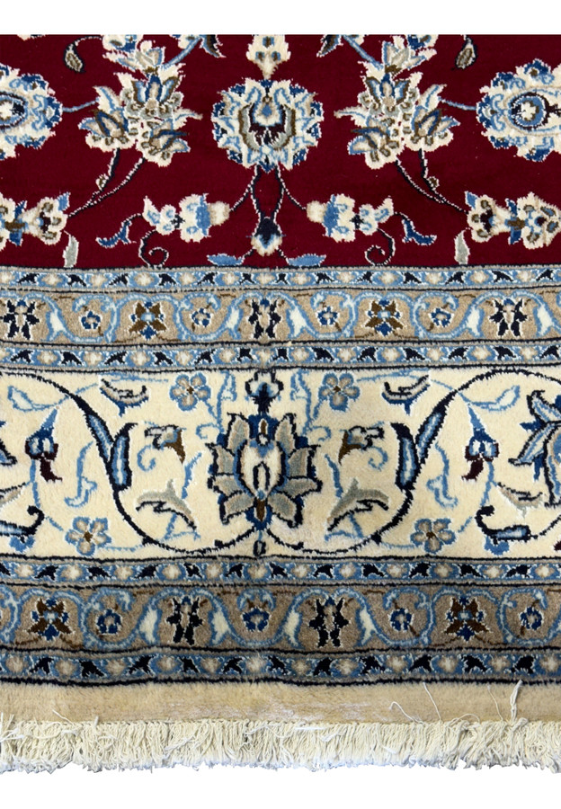 Macro shot focusing on the detailed floral and vine embroidery in the center of the Persian Nain 9La rug with highlights in silk, set against a deep red wool background