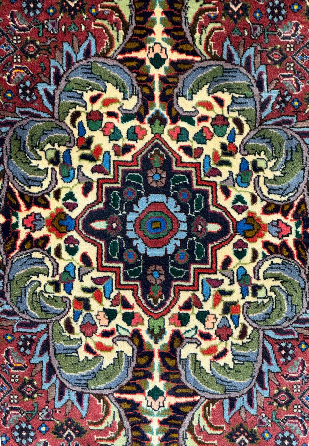 Detailed view of the medallion on the Persian Bidjar rug: This image provides a focused view of the central medallion, highlighting the complex design and vibrant color palette that includes shades of red, yellow, green, blue, and black.