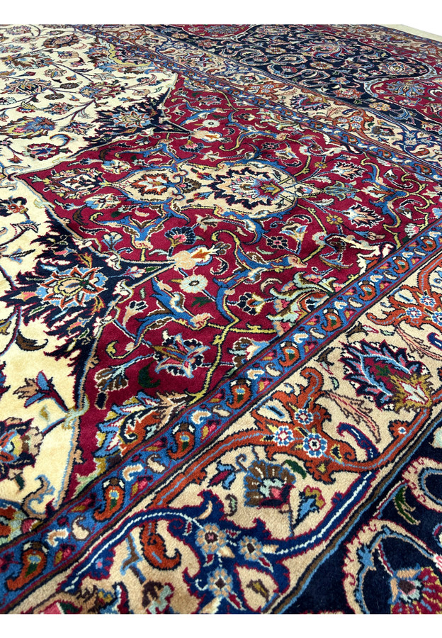 Close-up of intricate patterns and vibrant colors on a Persian Mashad rug, featuring detailed floral and vine motifs in red, blue, ivory, and gold, with exceptional craftsmanship and traditional Persian design elements
