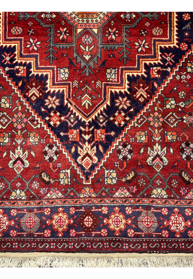 Detailed view of the left corner of a 3'4" x 5'1" Persian Gholtogh Rug. The intricate geometric and floral patterns in vibrant red and navy blue, combined with pastel accents, highlight the meticulous hand-knotted craftsmanship and traditional Persian design
