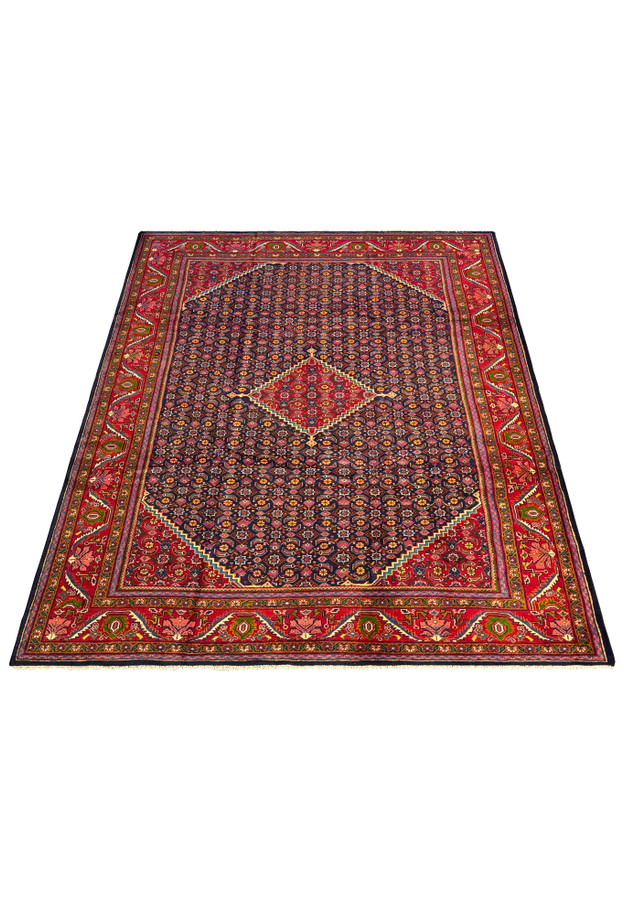 Angled perspective of a Persian Mahal Rug, highlighting the detailed craftsmanship and the harmonious color palette of navy, red, and gold. The view emphasizes the rug's intricate floral and geometric patterns, which are meticulously hand-knotted to create a dense, plush pile. This perspective showcases the rug's overall design, including the central medallion and the richly decorated borders, making it a standout piece in any room.