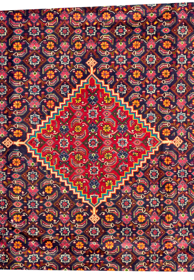 Close-up of the central medallion of a Persian Mahal Rug, featuring complex floral designs in a vibrant red and navy background. The detailed craftsmanship of the hand-knotted wool is evident in the intricate patterns and vibrant colors. This close-up allows for an appreciation of the fine details and the harmonious use of color that is characteristic of high-quality Mahal rugs, making it a focal point in any space