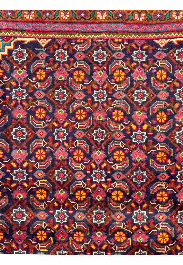 Detailed view of the floral motifs and geometric patterns in the central field of a Persian Mahal Rug, emphasizing the rich color contrast. The navy background is adorned with vibrant red, gold, and green floral designs, creating a visually appealing and intricate pattern. This close-up showcases the meticulous hand-knotting and the quality of the wool, reflecting the high craftsmanship and traditional artistry of Persian Mahal rugs.