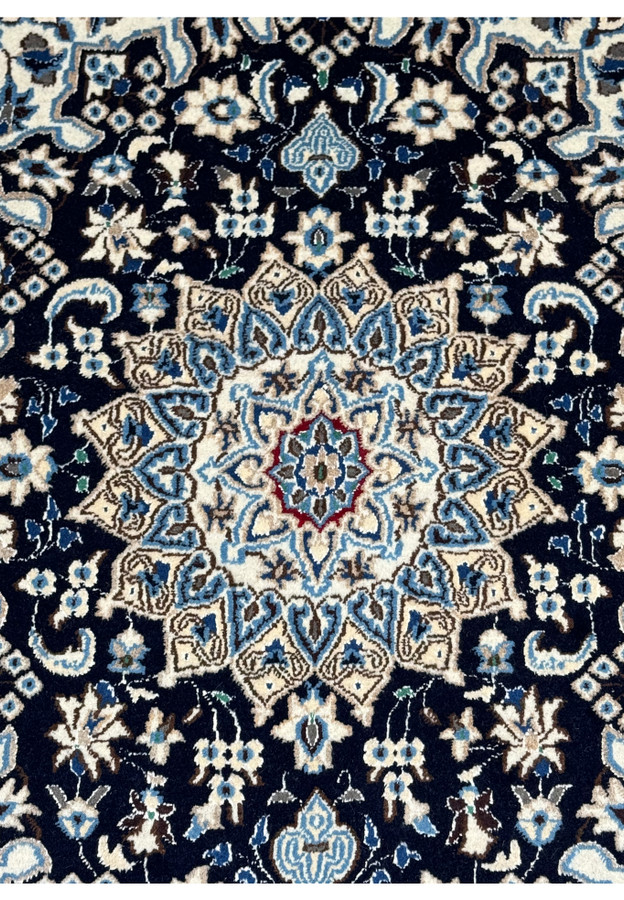 Close-up of the central medallion on a Persian Nain rug with intricate floral patterns in navy blue and ivory.