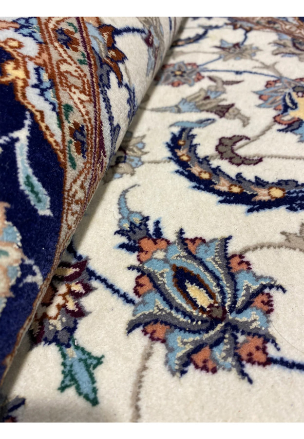 Close-up of Persian Isfahan runner rolled to show soft ivory wool field with blue and rust floral patterns.