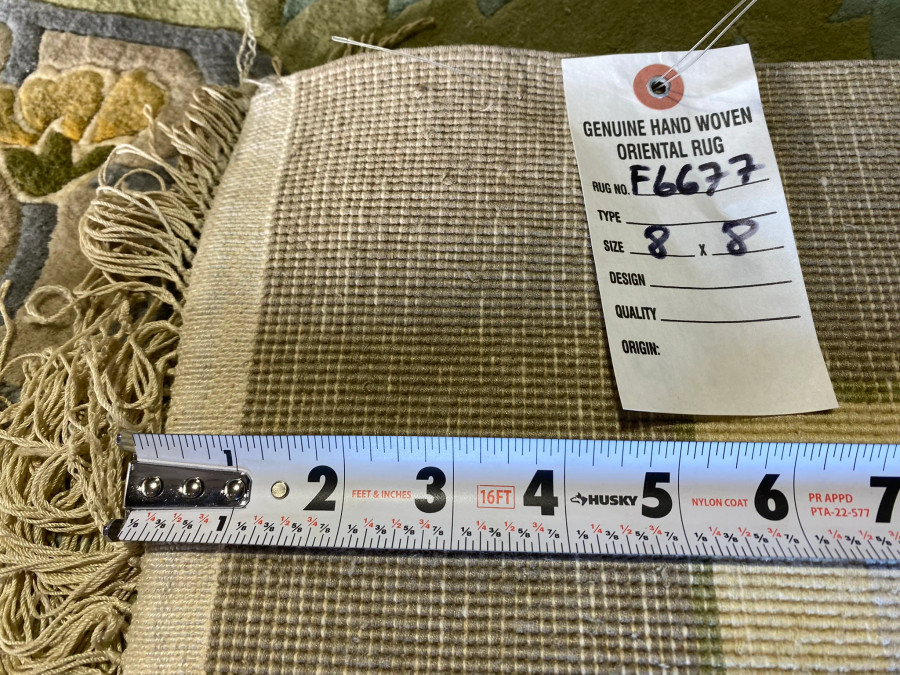 Close-up view of the backside of an 8x8 Vintage Oriental Art Deco Square Rug showing the woven foundation, beige fringe detailing, measuring tape for scale, and an attached label reading Genuine Hand Woven Oriental Rug confirming its handmade authenticity.