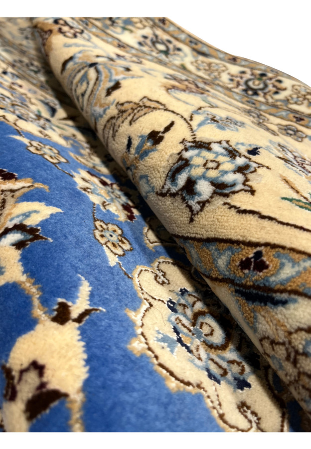 Rolled 6'7" × 9'8" Royal Blue Persian Nain 6 LA rug showing soft wool texture, ivory floral borders, and elegant blue field woven with fine silk highlights.